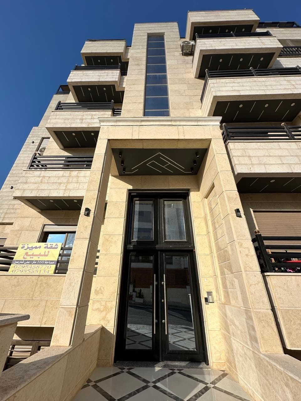المدخل الرئيسي لعمارة البنيات بإطار حجري وباب زجاجي مزدوج